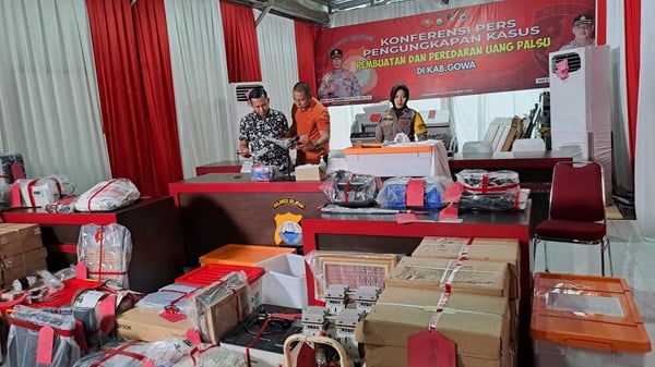 sejumlah barang bukti yang ditemukan dalam kasus pencetakan uang palsu di UIN Alauddin Makassar. Terlihat mesin pencetak uang, kertas khusus, dan tinta yang digunakan untuk memproduksi uang palsu. Kasus ini melibatkan sejumlah tersangka, termasuk Dr. Andi Ibrahim, Kepala UPT Perpustakaan UINAM, yang mengawasi proses produksi uang palsu. Mesin pencetak uang palsu yang canggih ini mampu menghasilkan uang dengan nilai tinggi dan sulit dideteksi oleh x-ray