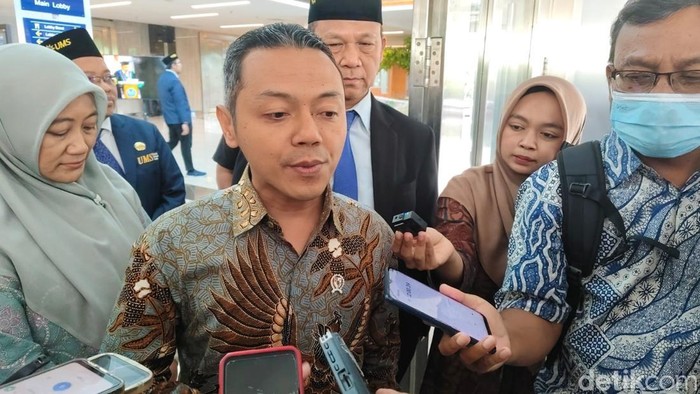 Gambar ini menampilkan seorang pejabat yang sedang memberikan pernyataan kepada media, dikelilingi oleh jurnalis dan rekan-rekannya, di mana ekspresinya mencerminkan keseriusan dalam menanggapi isu penting terkait kebijakan gizi gratis di sekolah.