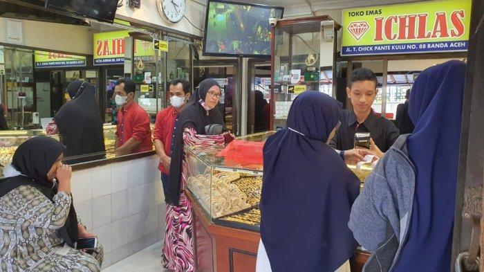 Suasana pasar emas di Banda Aceh yang ramai, dengan pedagang dan pembeli yang antusias. Di latar belakang, papan harga menunjukkan lonjakan signifikan pada harga emas hari ini. Momen ini mencerminkan ketertarikan masyarakat terhadap investasi emas yang semakin meningkat, seiring dengan berita harga yang mencetak rekor baru.