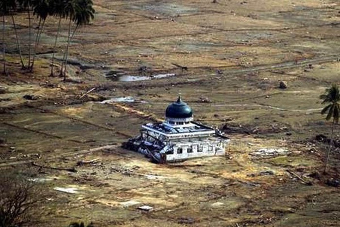Gambar ini menunjukkan sebuah masjid yang tetap berdiri di antara puing-puing dan tanah kosong pasca tsunami Aceh, mencerminkan tantangan pemulihan pendidikan dan infrastruktur yang dihadapi dua dekade setelah bencana menghancurkan tersebut.