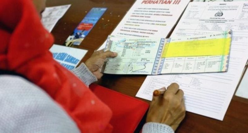 seseorang yang sedang mengurus dokumen kendaraan di kantor Samsat, dengan latar belakang berbagai formulir dan petugas yang sedang melayani