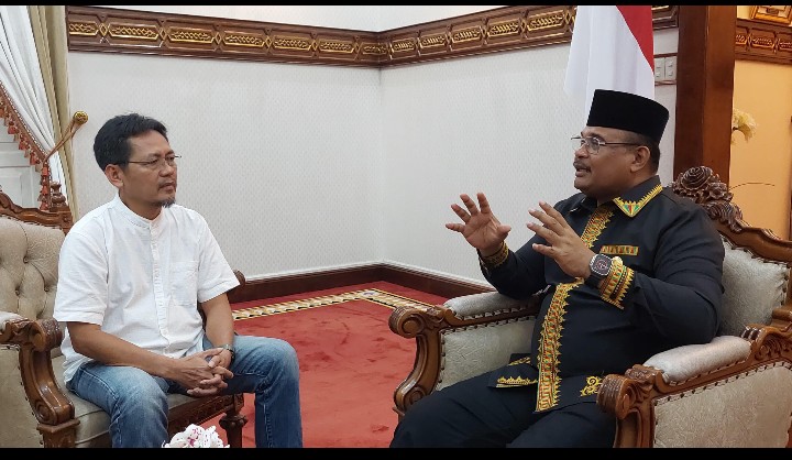 Pj Gubernur Safrizal berbincang serius dengan seorang tokoh masyarakat, membahas strategi investasi sebagai motor penggerak ekonomi Aceh yang terhambat.