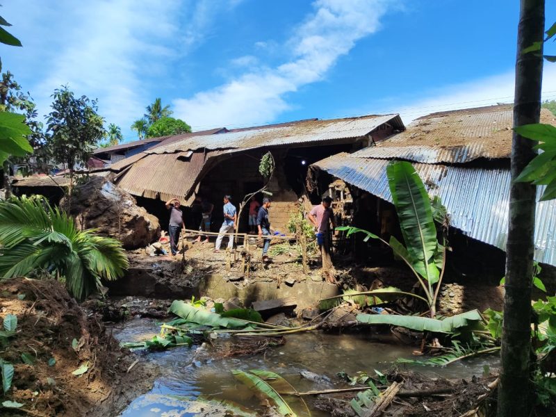 Dalam gambar ini, terlihat kerusakan parah pada lima rumah yang hancur akibat longsoran batu. Tim penyelamat dan warga setempat sedang berupaya mengevakuasi puing-puing dan mencari korban.